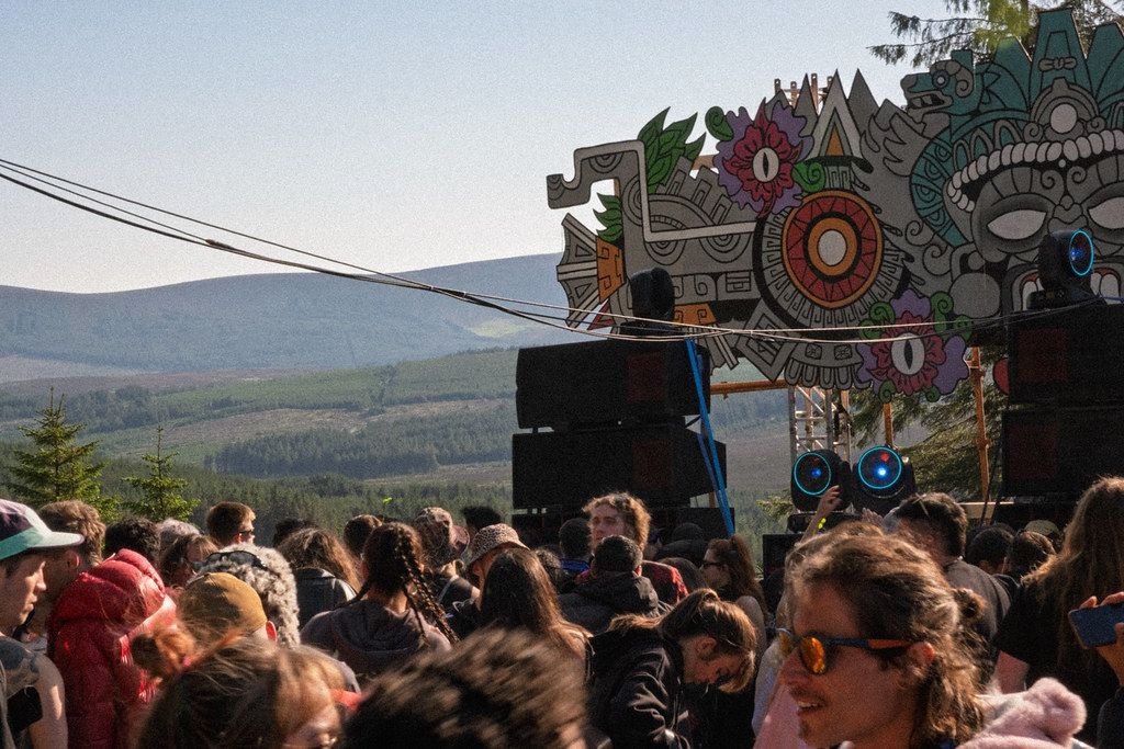 Daytime festival crowd with mountains and art stage